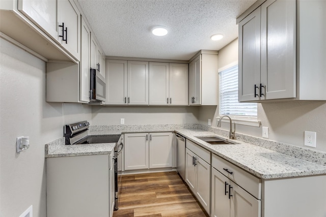 kitchen with light stone counters, stainless steel appliances, light wood-style flooring, a sink, and a textured ceiling