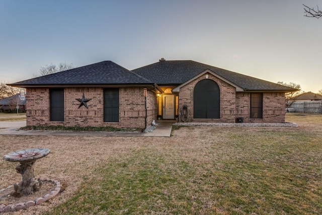 view of front of property with brick siding, a lawn, and a shingled roof