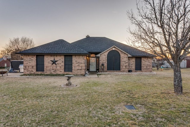 view of front facade with a shingled roof, a lawn, and brick siding