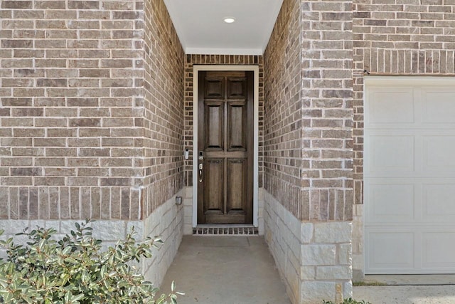 entrance to property featuring a garage and brick siding