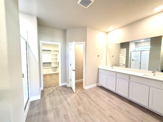 bathroom with wood finish floors, a sink, visible vents, a spacious closet, and a stall shower