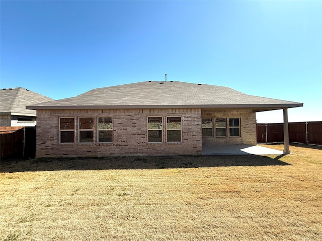 back of property featuring a shingled roof, a lawn, fence, a patio area, and brick siding