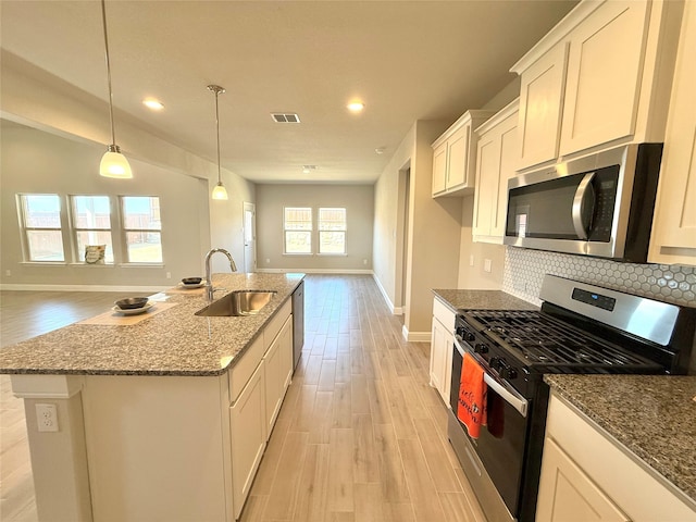 kitchen with appliances with stainless steel finishes, open floor plan, a kitchen island with sink, a sink, and white cabinetry