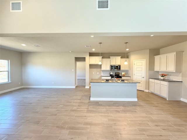 kitchen with visible vents, an island with sink, open floor plan, stainless steel appliances, and white cabinetry