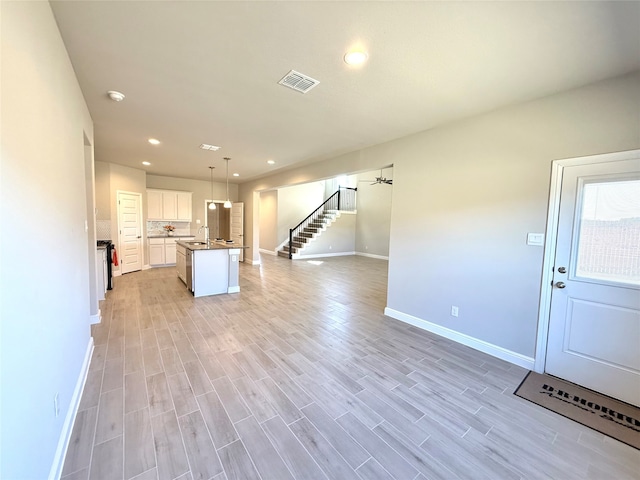 kitchen featuring a center island with sink, visible vents, open floor plan, hanging light fixtures, and white cabinetry