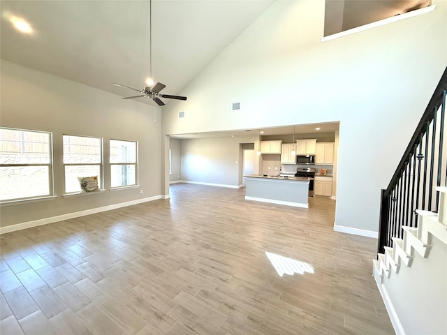 unfurnished living room featuring light wood-style flooring, stairs, baseboards, and ceiling fan