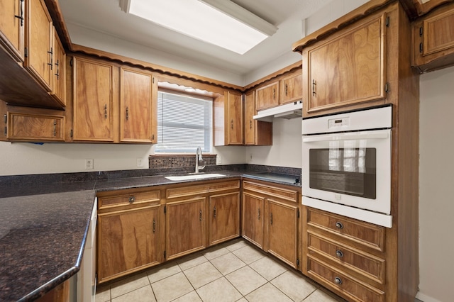 kitchen with brown cabinets, light tile patterned flooring, a sink, oven, and under cabinet range hood