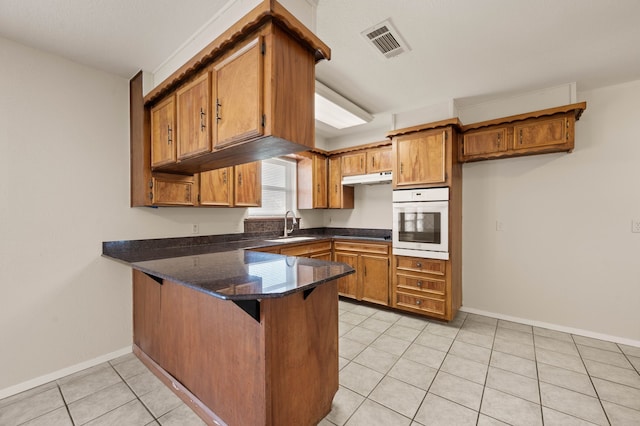 kitchen featuring white oven, brown cabinetry, a sink, visible vents, and a peninsula