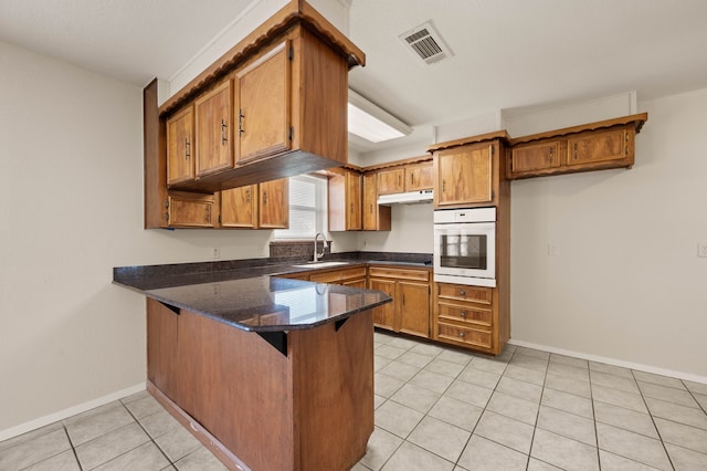 kitchen with visible vents, brown cabinetry, a sink, oven, and a peninsula