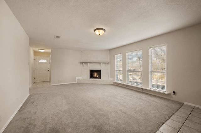 unfurnished living room featuring a textured ceiling, carpet, visible vents, and a brick fireplace