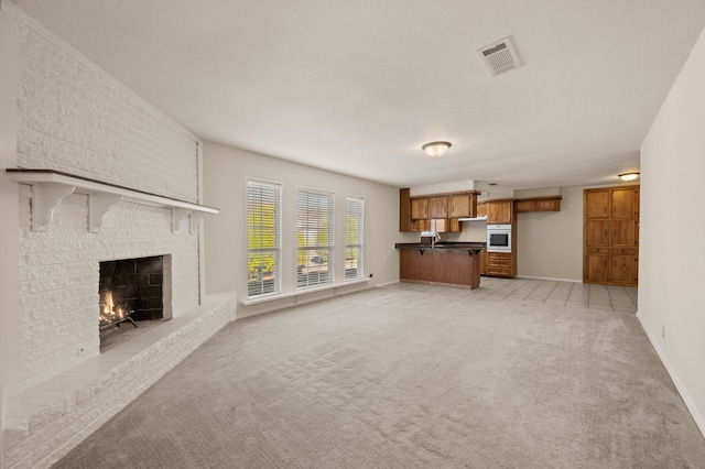 unfurnished living room with visible vents, a brick fireplace, light carpet, a sink, and baseboards