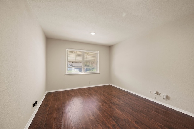 spare room with dark wood-type flooring, a textured wall, a textured ceiling, and baseboards