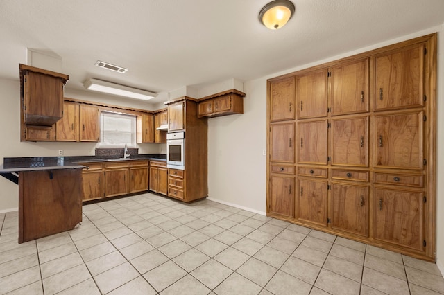 kitchen with a sink, brown cabinetry, visible vents, a peninsula, and white oven