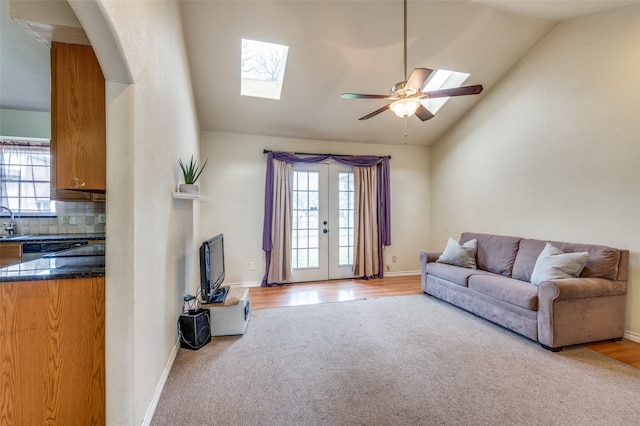 living room featuring vaulted ceiling with skylight, french doors, light colored carpet, and baseboards