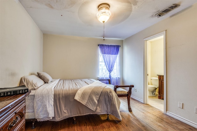 bedroom featuring visible vents, a ceiling fan, ensuite bath, wood finished floors, and baseboards