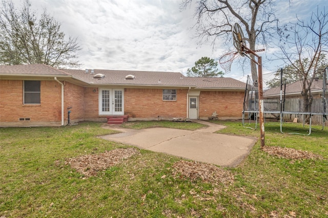 rear view of house with a patio, brick siding, a yard, french doors, and a trampoline