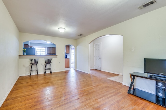 living room featuring arched walkways, light wood-style flooring, visible vents, and baseboards