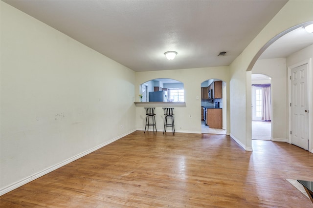 unfurnished living room with arched walkways, baseboards, a healthy amount of sunlight, and light wood finished floors