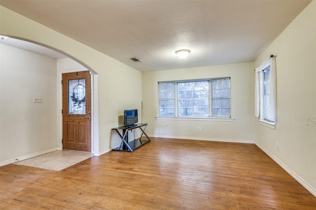 foyer entrance featuring arched walkways, light wood-style flooring, visible vents, and baseboards