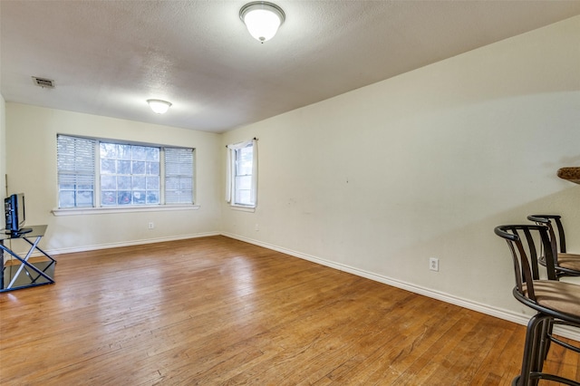 empty room featuring a textured ceiling, wood finished floors, visible vents, and baseboards