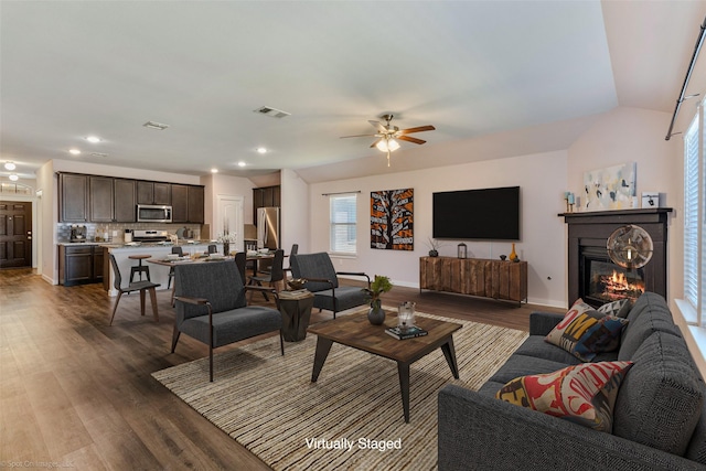 living room with lofted ceiling, dark wood finished floors, visible vents, a ceiling fan, and a glass covered fireplace