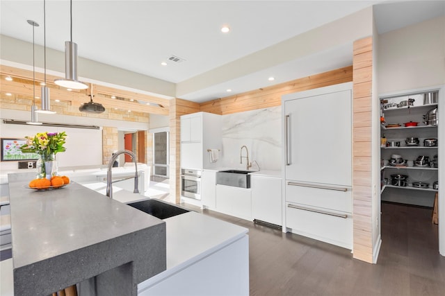 kitchen with oven, a sink, white cabinetry, hanging light fixtures, and dark wood finished floors