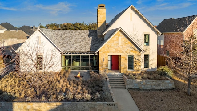 view of front facade featuring roof with shingles, a chimney, stucco siding, stone siding, and a fire pit