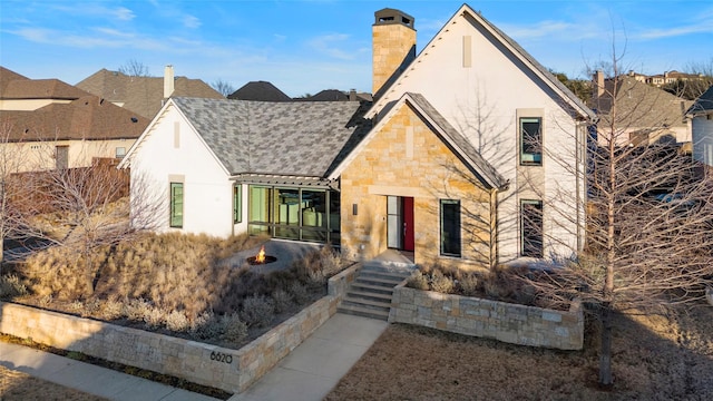 view of front of property featuring a shingled roof, stone siding, a chimney, and stucco siding