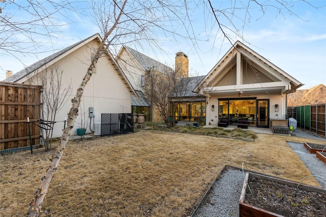 back of house with a vegetable garden, a lawn, a chimney, fence, and stucco siding