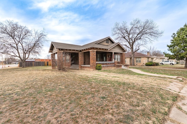 view of front of house featuring brick siding, a porch, a front yard, and fence