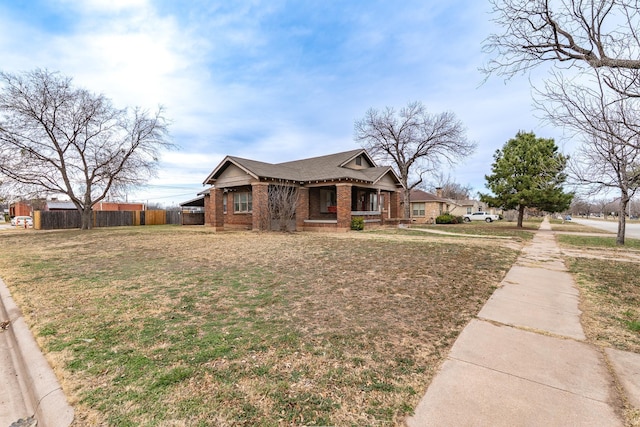 view of front of property with covered porch, fence, a front lawn, and brick siding