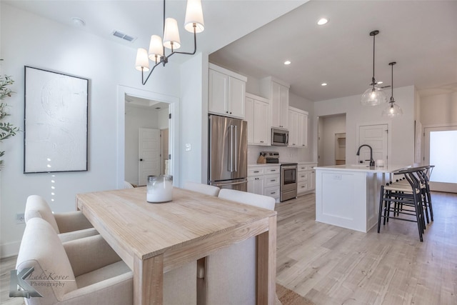 kitchen featuring stainless steel appliances, light countertops, white cabinetry, and a center island with sink