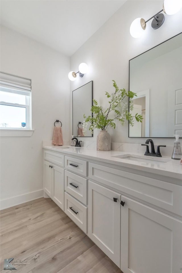 full bath featuring wood finished floors, a sink, baseboards, and double vanity