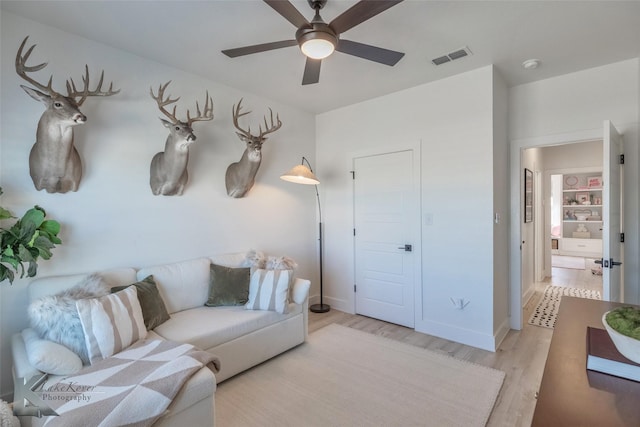 living room with light wood-style floors, ceiling fan, visible vents, and baseboards