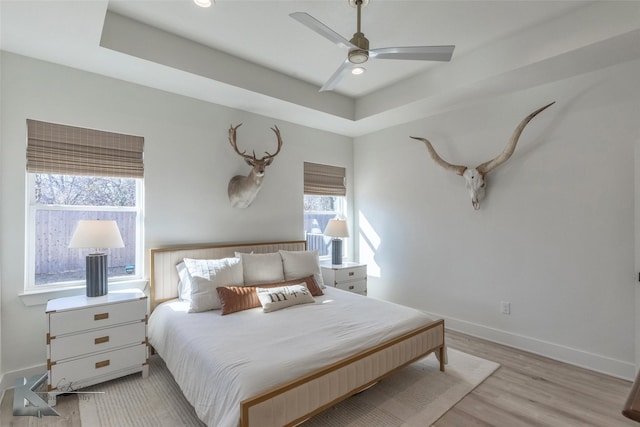 bedroom featuring light wood finished floors, recessed lighting, a raised ceiling, and baseboards