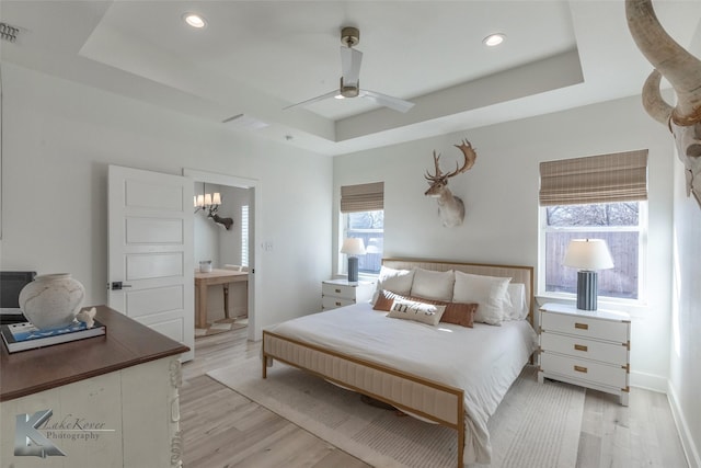 bedroom with light wood-type flooring, a raised ceiling, and recessed lighting