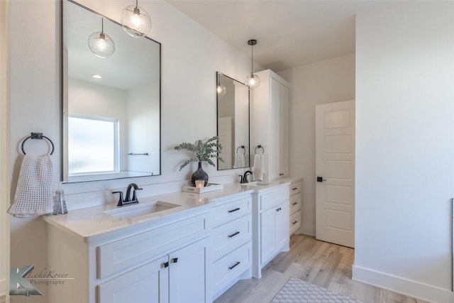 full bath featuring double vanity, a sink, baseboards, and wood finished floors