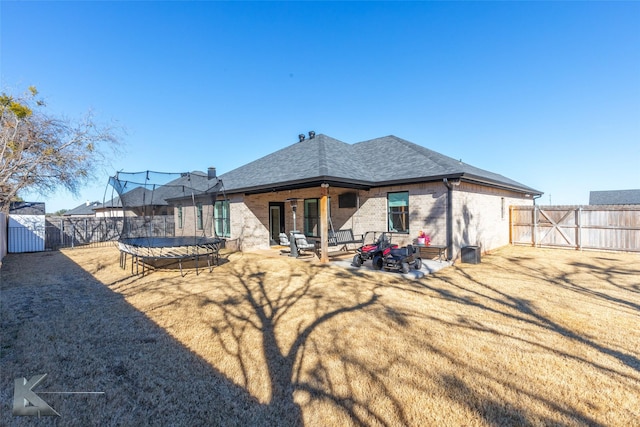 rear view of property featuring a patio, a fenced backyard, brick siding, a gate, and a trampoline