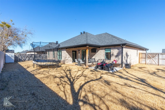 rear view of property featuring a fenced backyard, brick siding, roof with shingles, a trampoline, and a patio area