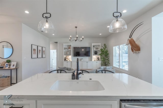 kitchen with light stone counters, open floor plan, a kitchen island with sink, pendant lighting, and a sink