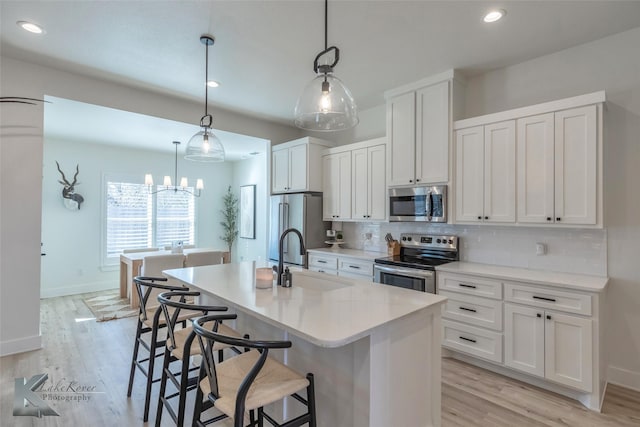 kitchen featuring a kitchen island with sink, stainless steel appliances, light countertops, white cabinetry, and a sink