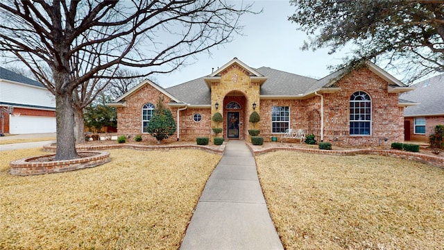 view of front facade featuring brick siding, a front lawn, and roof with shingles