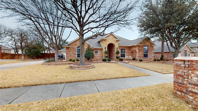 view of front facade featuring brick siding, a front yard, fence, and a shingled roof