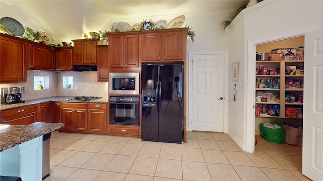 kitchen featuring light tile patterned floors, dark stone counters, decorative backsplash, under cabinet range hood, and black appliances