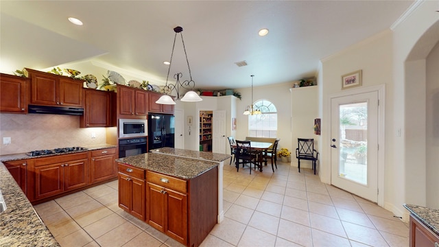 kitchen with under cabinet range hood, decorative backsplash, black appliances, dark stone countertops, and decorative light fixtures