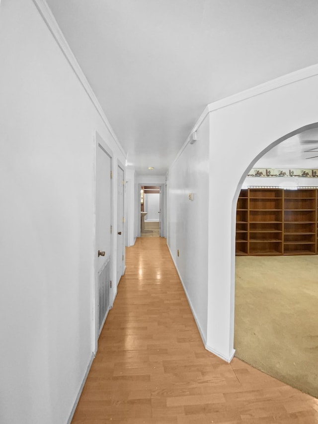 corridor featuring arched walkways, crown molding, light wood-style flooring, and baseboards