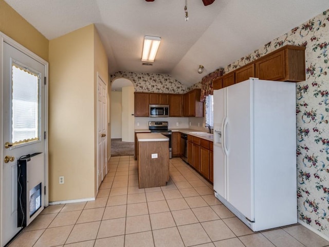 kitchen with stainless steel appliances, lofted ceiling, light tile patterned flooring, and wallpapered walls