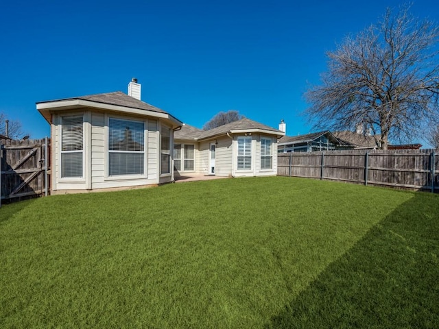 rear view of house featuring a yard, a fenced backyard, and a chimney