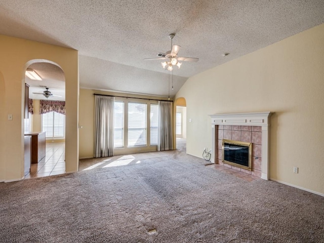 unfurnished living room featuring a tiled fireplace, lofted ceiling, carpet flooring, arched walkways, and a ceiling fan