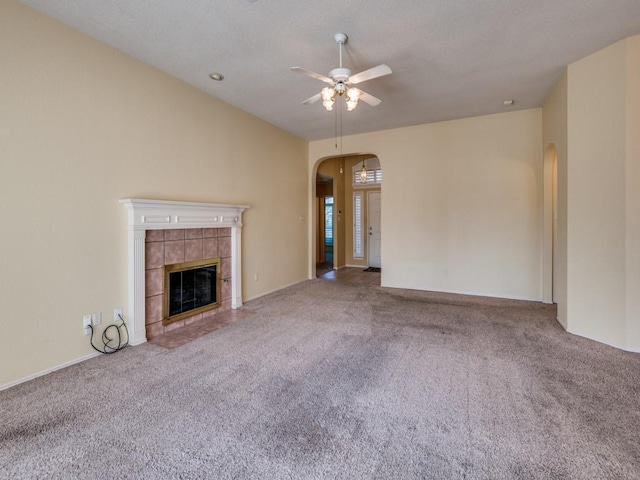 unfurnished living room with arched walkways, carpet flooring, a tile fireplace, and a ceiling fan